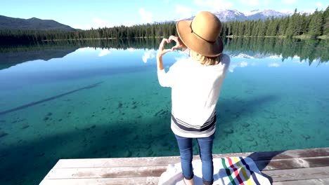 Mujer-joven-en-muelle-de-madera-hace-forma-marco-de-corazón-en-la-naturaleza