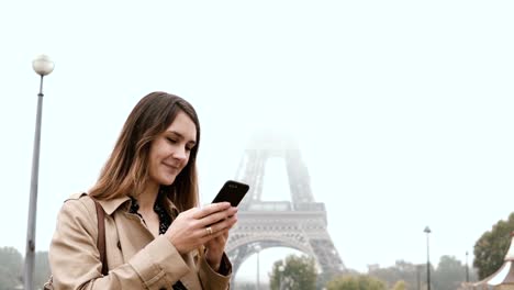 Junge-schöne-Frau-zu-Fuß-nahe-des-Eiffelturms-in-Paris,-Frankreich-im-nebligen-Morgen.-Weibchen-mit-dem-smartphone