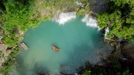 Drone-shot-aerial-view-of-young-woman-bamboo-rafting-at-tropical-waterfall.-4K-resolution-video,-shot-in-the-Philippines.-People-travel-fun-vacations-adventure-concept