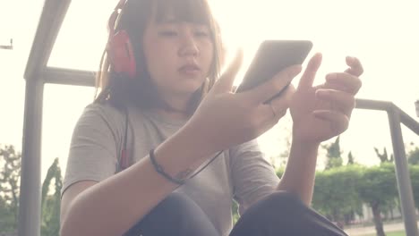 Schöne-junge-asiatische-Frau-anhören-von-Musik-auf-einem-Smartphone-in-der-Stadt.-Junge-asiatische-Frau,-entspannende-Musik-hören-auf-der-Straße.