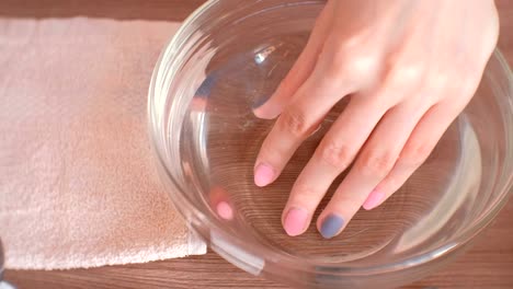 Manicura-en-casa.-Mujer-que-sumerge-su-mano-en-un-recipiente-de-agua.-Primer-plano-de-la-mano.