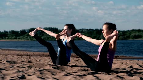 Two-woman-doing-yoga-on-the-beach-by-the-river-in-the-city.-Beautiful-view-in-city.