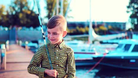 Little-boy-with-a-fishing-rod-is-standing-on-a-dock-near-boats-and-yachts