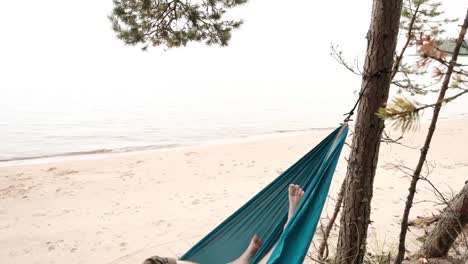 Young-caucasian-male-resting-lying-on-blue-hammock-outdoors-near-lake.