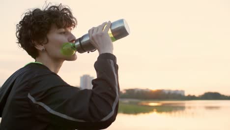 Deportiva-mujer-bebiendo-agua-y-disfrutando-de-amanecer