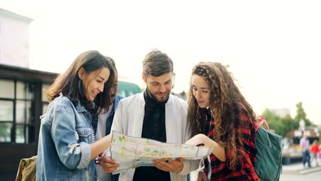 Young-men-and-women-with-backpacks-are-looking-at-map-standing-in-the-street-in-foreign-city-and-talking-discussing-journey.-Navigation,-youth-and-tourism-concept.