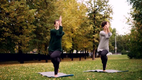 Slender-girl-yoga-student-is-learning-Eagle-pose-under-guidance-of-teacher-during-individual-practice-with-instructor-in-park.-Beautiful-autumn-nature-is-in-background.