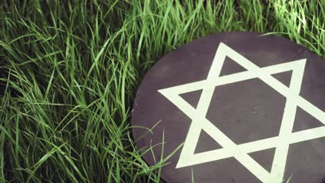 White-Star-of-David-on-a-black-stone-round-on-a-grass-background,-rotation-360-degrees.