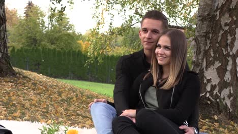 A-young-couple-sits-on-a-white-bedspread-in-autumn-park