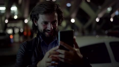 Hombre-sonriente-para-hacer-video-llamada-en-teléfono-inteligente-en-la-ciudad-de-noche