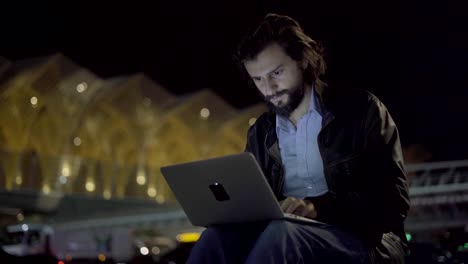 Young-confident-man-typing-on-laptop-in-night-city