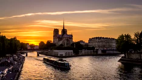 Timelapse-of-boats-in-Paris-at-sunset,-with-Notre-Dame-De-Paris-church-in-the-background-and-people-resting-on-the-docks,-view-from-Tournelle-bridge