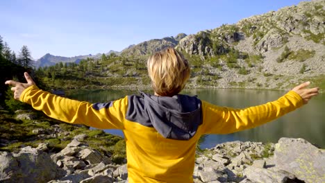 Joven-excursionista-en-ruta-en-verano-por-el-impresionante-lago-alpino-brazos-extendidos-celebrando-personal-objetivo.-Hombre-joven-de-pie-en-la-naturaleza-amplia-de-brazos-abiertos