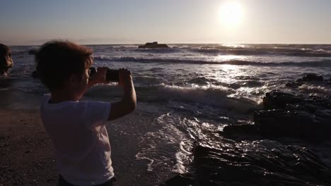 Junge-mit-Smartphone,-die-eine-Aufnahme-am-Strand-Kapstadt,-Südafrika