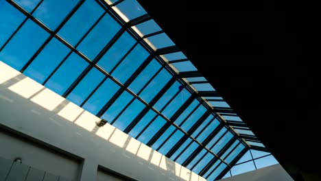 Schwenk-in-der-Glasdecke-des-Einkaufszentrums-auf-einem-Hintergrund-von-Time-Lapse-Licht-der-Sonnenstrahlen-auf-einen-blauen-Himmel