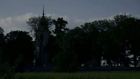 Tiro-largo-a-la-pequeña-iglesia-con-campanario-y-cementerio,-raging-velas-sobre-las-tumbas.