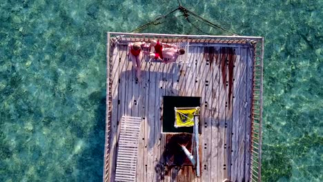 v03824-fliegenden-Drohne-Luftaufnahme-der-Malediven-weißen-Sandstrand-2-Personen-junges-Paar-Mann-Frau-entspannend-auf-sonnigen-tropischen-Inselparadies-mit-Aqua-blau-Himmel-Meer-Wasser-Ozean-4k-schwimmenden-Ponton-Steg-Sonnenbaden-zusammen