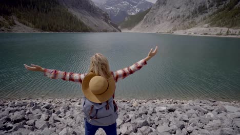 Young-woman-hiker-arms-outstretched-at-mountain-lake