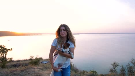 Mujer-atractiva-joven-jugando-con-un-perro-Jack-Russell-en-el-Prado-al-atardecer-con-el-fondo-del-mar.-cámara-lenta