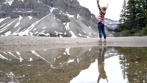 Young-woman-stands-by-beautiful-mountain-lake-scenery-with-her-arms-wide-open
