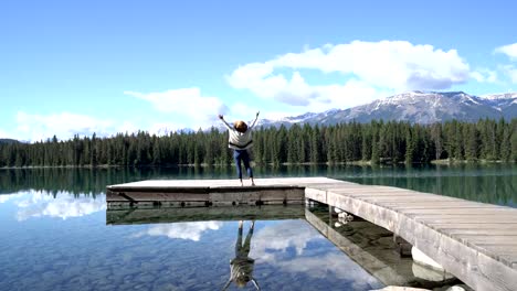 Junge-Frau-steht-auf-hölzerne-Pier-von-herrlichen-Bergsee-mit-ihre-Arme-weit-öffnen,-um-die-Natur-zu-umarmen