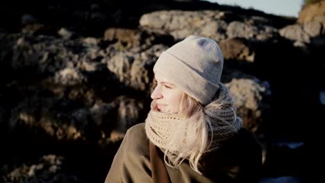 Portrait-of-young-beautiful-woman-standing-near-the-mountain-and-looking-around,-hair-waving-on-wind-in-sunny-day