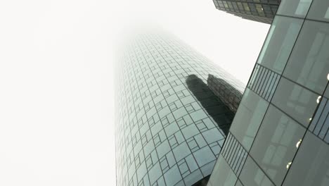 Driving-Directly-Below-Glass-Skyscraper-and-White-Sky