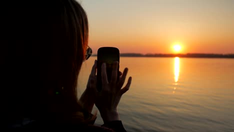 Mädchen-übernimmt-Bilder-von-traumhaften-Sonnenuntergang-und-Fluss-Böschung-durch-ihr-modernes-Mobiltelefon