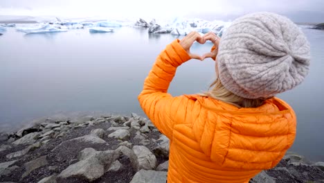 Junge-Frau-macht-Herz-Form-Finger-Frame-auf-Gletscherlagune-in-Island