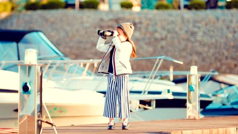 Pequeña-y-hermosa-niña-mira-a-través-de-binoculares-en-el-muelle-para-barcos-y-yates