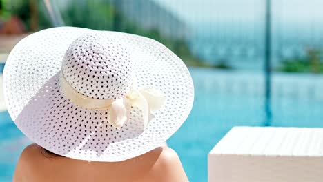 Rear-view-woman-in-elegant-sun-hat-enjoying-vacation-sunbathing-and-drinking-red-wine