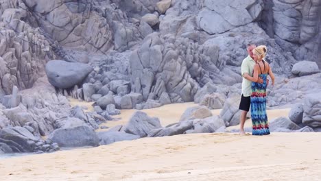 Una-Pareja-de-ancianos-beso-en-la-playa,-en-frente-de-gran-rocas