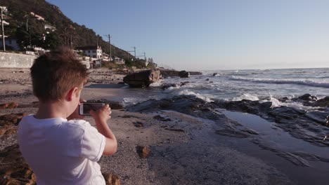 Junge-mit-Smartphone,-die-eine-Aufnahme-am-Strand-Kapstadt,-Südafrika