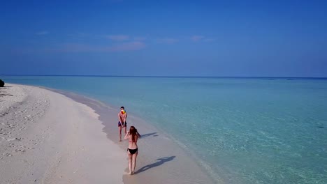 v03818-Aerial-flying-drone-view-of-Maldives-white-sandy-beach-on-sunny-tropical-paradise-island-with-aqua-blue-sky-sea-water-ocean-4k-2-people-young-couple-man-woman-playing-ball-fun-together