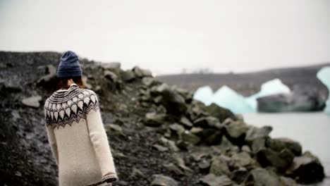 Young-traveling-woman-walking-through-the-rocks-in-Jokulsalon-ice-lagoon-in-Iceland-alone,-exploring-the-sight