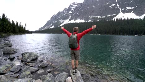 Hiker-celebrating-by-mountain-lake,-4K