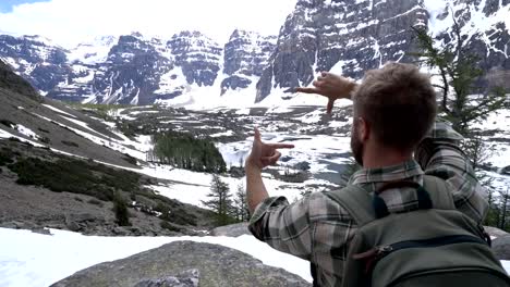 Man-hiker-reaches-mountain-top-and-frames-beautiful-mountain-scenery-with-hands