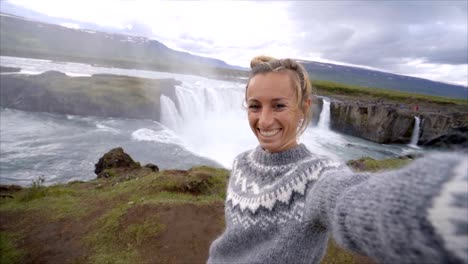 Slow-motion--Young-woman-taking-selfie-portrait-with-magnificent-waterfall-in-Iceland,-Godafoss-falls.-People-travel-exploration-concept