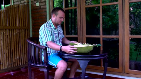 Ein-Mann-sitzt-auf-der-Terrasse-und-die-Jackfruit-mit-einem-Messer-schneidet