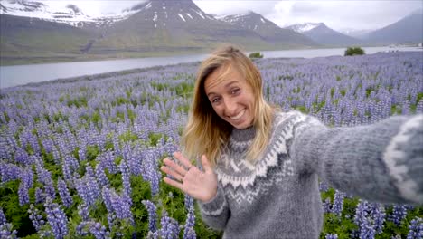 Selfie-retrato-de-mujer-de-turismo-en-Islandia-en-medio-de-flores-de-color-púrpura-Lupine,-sonriente-de-pelo-en-el-viento,-plazas-de-lana