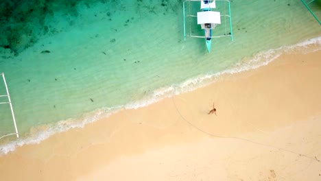 Drone-shot-aerial-view-of-young-woman-walking-on-idyllic-tropical-beach