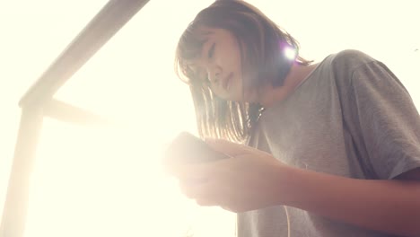 Beautiful-young-asian-woman-listening-to-music-on-a-smart-phone-in-the-city.-Young-asian-woman-relaxing-listening-to-music-on-the-street.