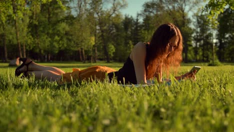 Happy-woman-type-sms-or-chat,-sitting-in-park-on-grass.-Woman-chatting-in-telephone