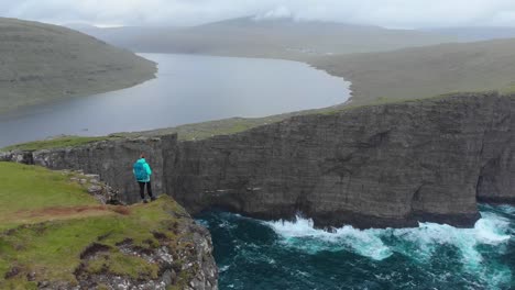 AERIAL:-Cheerful-female-hiker-raises-her-arms-after-walking-up-to-edge-of-cliff.