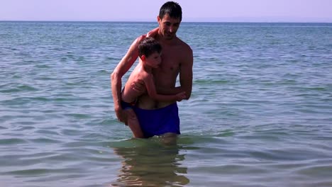 Joven-padre-con-un-hijo-pequeño-en-la-playa-de-la-mar,-Grecia