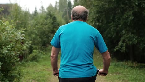 Senior-caucasian-male-in-blue-t-shirt-enjoying-his-summer-vacation-riding-a-bicycle-outdoor-between-trees.