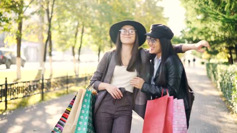 Feliz-mujeres-jóvenes-amigos-están-hablando,-riendo-y-abrazando-a-pie-en-la-calle-con-bolsas-de-papel,-compartiendo-noticias.-Compras,-la-amistad-y-concepto-de-la-gente.