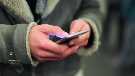 Commuter-person-holding-cellphone-device-browsing-the-internet-on-smartphone-checking-emails-texting-friends-while-on-underground-subway-platform-in-4K