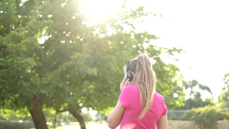 Teenage-girl-listening-to-the-music-in-the-park,-lens-flare-background