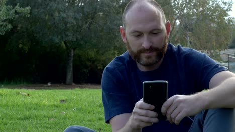 Bärtiger-Mann-mit-Smartphone,-sitzen-im-park